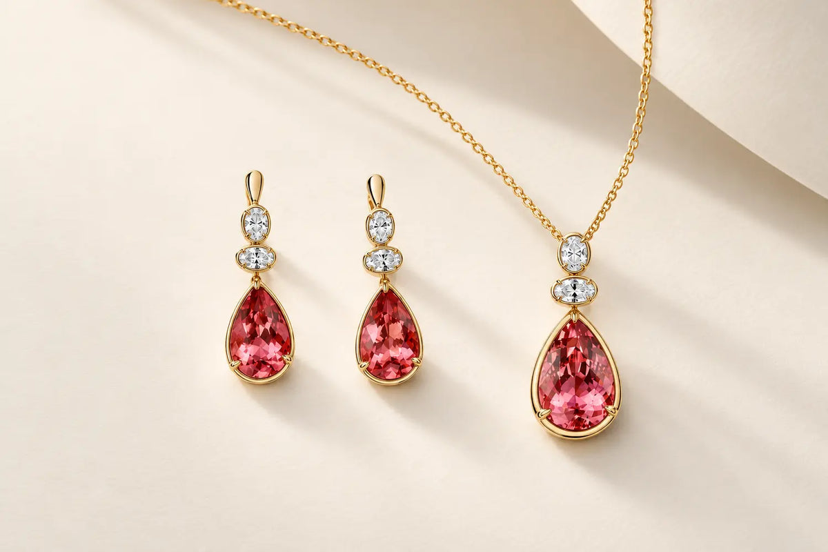 Matching yellow gold pendant and drop earrings with pear-shaped pink gemstones and oval diamonds on an ivory background
