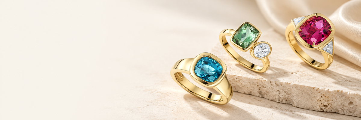 Blue, green and pink gemstone rings arranged on pale stone